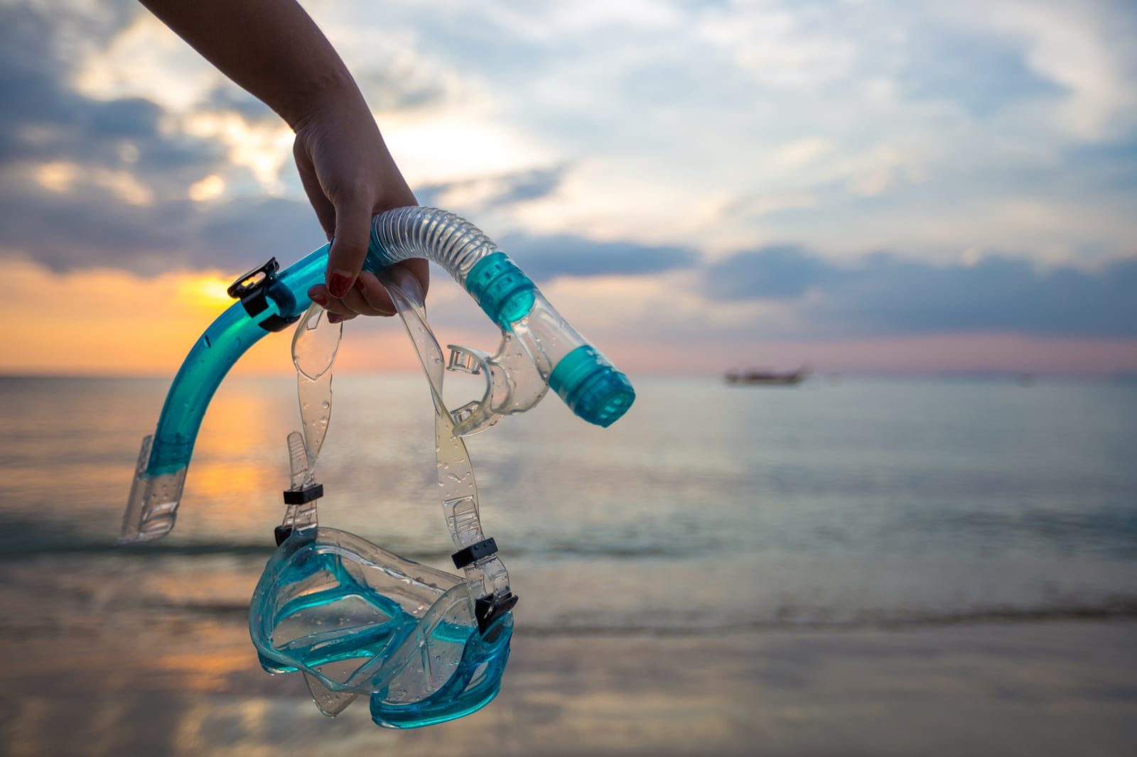 Mão segurando um snorkel e uma máscara contra o horizonte do mar ao entardecer